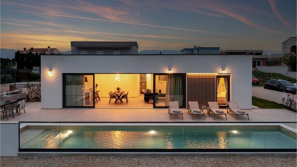 Een modern huis met een zwembad, een eethoek en een loungeruimte met zitplaatsen buiten.