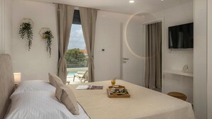 Een moderne hotelkamer met een bed, een televisie, een balkon met uitzicht op het zwembad, en een eethoek met een dienblad eten.