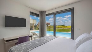 Ein modernes Hotelzimmer mit einem großen Bett, einem Schreibtisch, einem Flachbildfernseher und Blick auf einen Pool und die Landschaft.