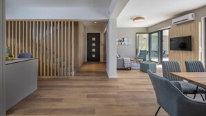 Ein modernes Interieur mit Holzboden, einer Essecke mit Tisch und Stühlen, einer Couch und einem an der Wand montierten Fernseher.