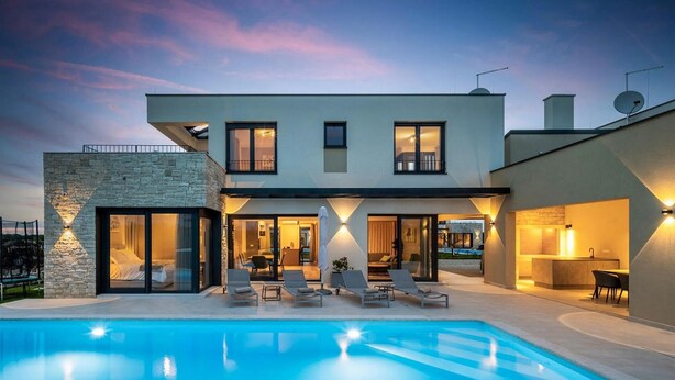 Ein modernes, zweistöckiges Haus mit Schwimmbad, großen Fenstern und Außenbeleuchtung.
