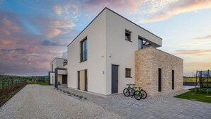 Ein modernes, zweistöckiges Haus mit flachem Dach, einem Balkon und einer Zuwegung mit Kies.