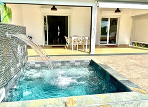 Una piscina con una cascata, una veranda coperta con posti a sedere all'aperto e vista sul paesaggio circostante.