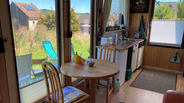 A cozy cabin with a dining area, kitchen, and a view of the surrounding landscape. - Tiny House Anneliese, Air Conditioning, E-Bikes, Dogs Welcome (Oberbettingen)