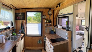 A compact kitchen with wooden cabinets, a sink, a toaster, and a window with blinds. - Tiny House Anneliese, Air Conditioning, E-Bikes, Dogs Welcome (Oberbettingen)