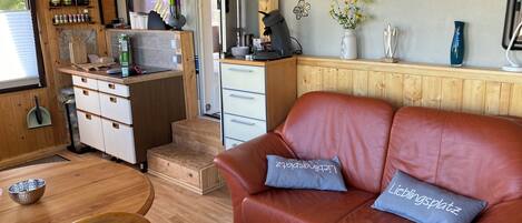 A compact RV interior with a kitchenette, a dining area, and a seating area with a leather couch and pillows.