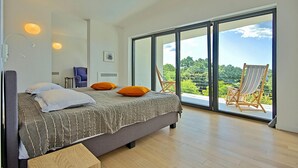 Une chambre moderne avec un grand lit, deux fauteuils et un balcon offrant une vue agréable.