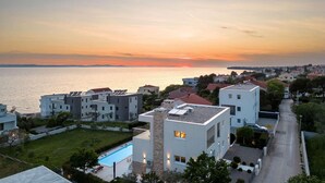 Ein Wohngebiet mit modernen Gebäuden, einem Schwimmbad und Blick auf das Meer bei Sonnenuntergang.
