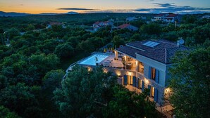 Una casa moderna con piscina, rodeada de abundante vegetación y colinas al fondo.