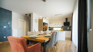 A modern dining area with a wooden table set for four, surrounded by chairs. A kitchen is visible in the background with a TV mounted above the counter. - Pet friendly home in Posedarje (Posedarje)