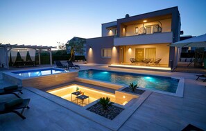 A modern two-story house with a swimming pool, outdoor seating, and a well-lit patio area. - Pet friendly home in Posedarje (Posedarje)