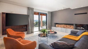 Ein modernes Wohnzimmer mit einem großen Flachbildfernseher, zwei orangefarbenen Sesseln, einem grauen Sofa und einem Kamin.
