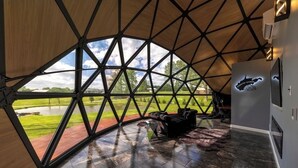 Un interior moderno y geométrico con un amplio ventanal que ofrece vistas a un paisaje verde y una masa de agua.