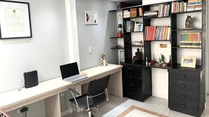 A modern office space with a desk, chair, bookshelf, and framed certificates on the wall. - Hab Nawi NF (Cali)