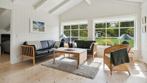 A spacious living room with a black leather sofa, a wooden coffee table, and a wicker chair. Large windows offer a view of a green garden. - Gorgeous home in Jerup with sauna (Jerup)