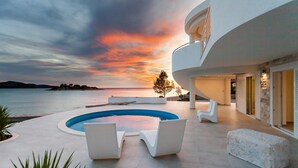 A modern building with a pool, outdoor seating, and a view of the sea at sunset. - Amazing home in Gradina (Gradina)