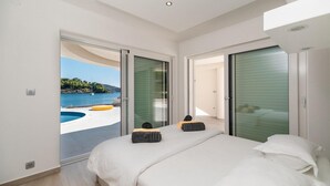 A modern bedroom with a large bed, a view of a swimming pool and sea, and sliding glass doors leading to an outdoor area. - Amazing home in Gradina (Gradina)