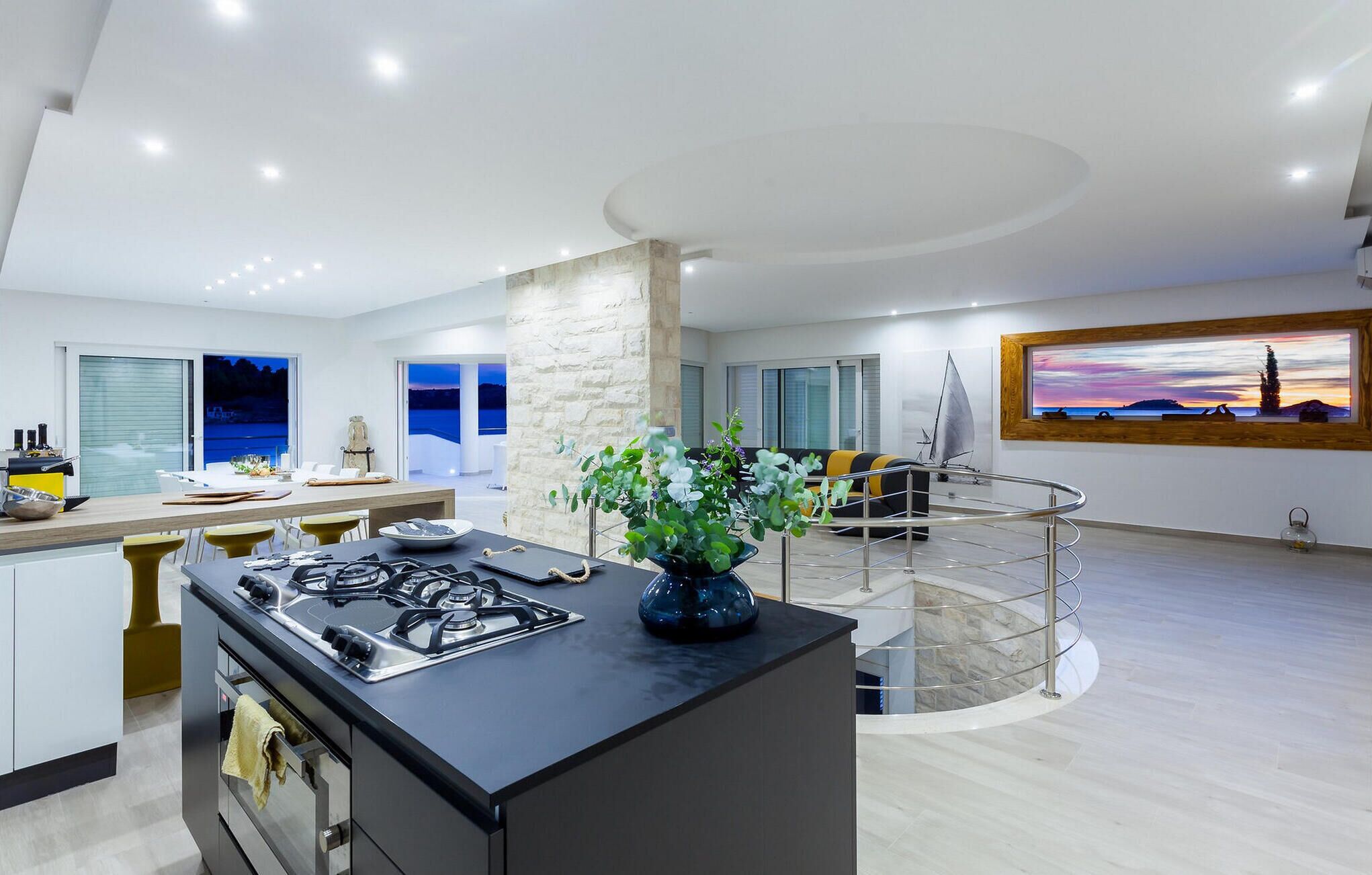 A modern kitchen with a central island, a dining area with a view, and a living space with a sailboat model.