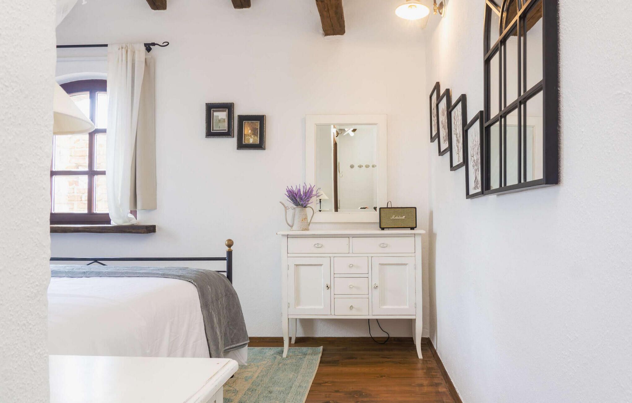 Une chambre à coucher avec un lit, une commode, un miroir et des tableaux encadrés accrochés au mur.