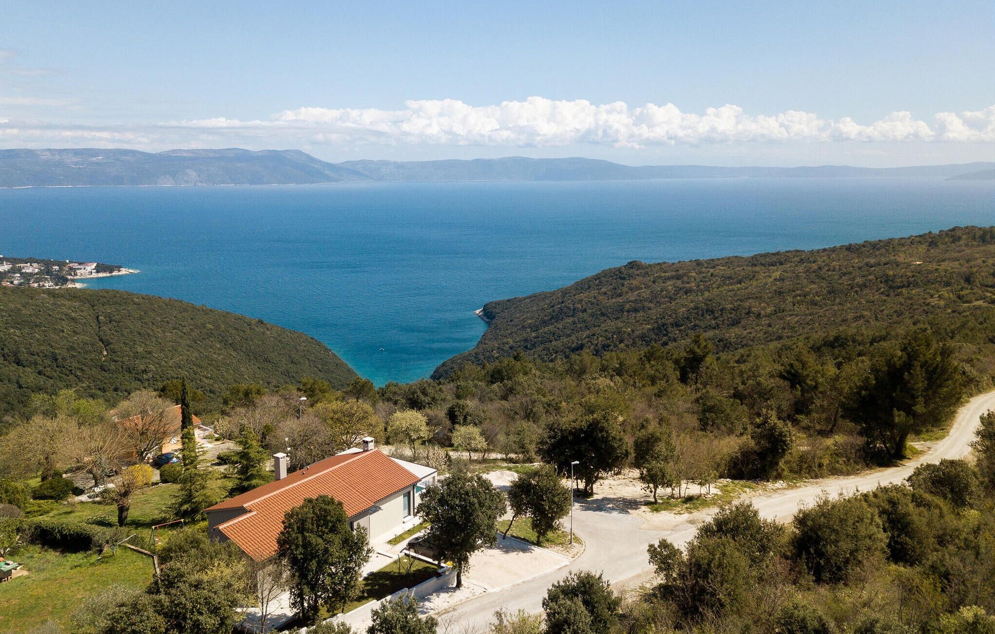 A coastal view with a house on a hillside, a road, and a distant shoreline.