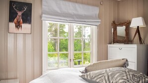 A bedroom with a large window, a bed with patterned pillows, a bedside table, and a framed picture of a deer. - 3 bedroom nice home in Gol (Gol)