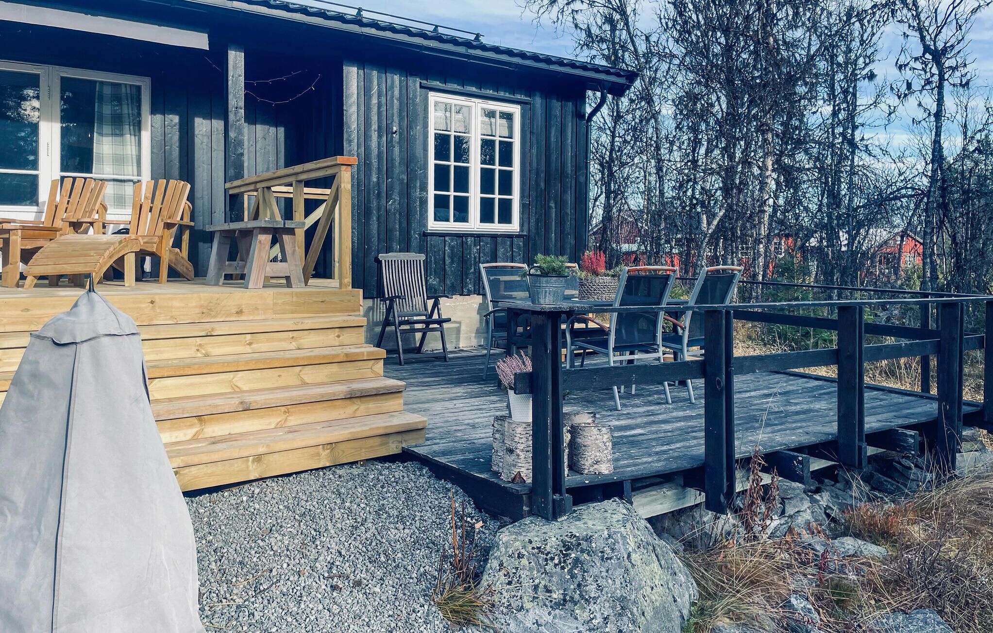 Una terraza de madera con mobiliario exterior, una zona de estar cubierta y vistas a un área boscosa.