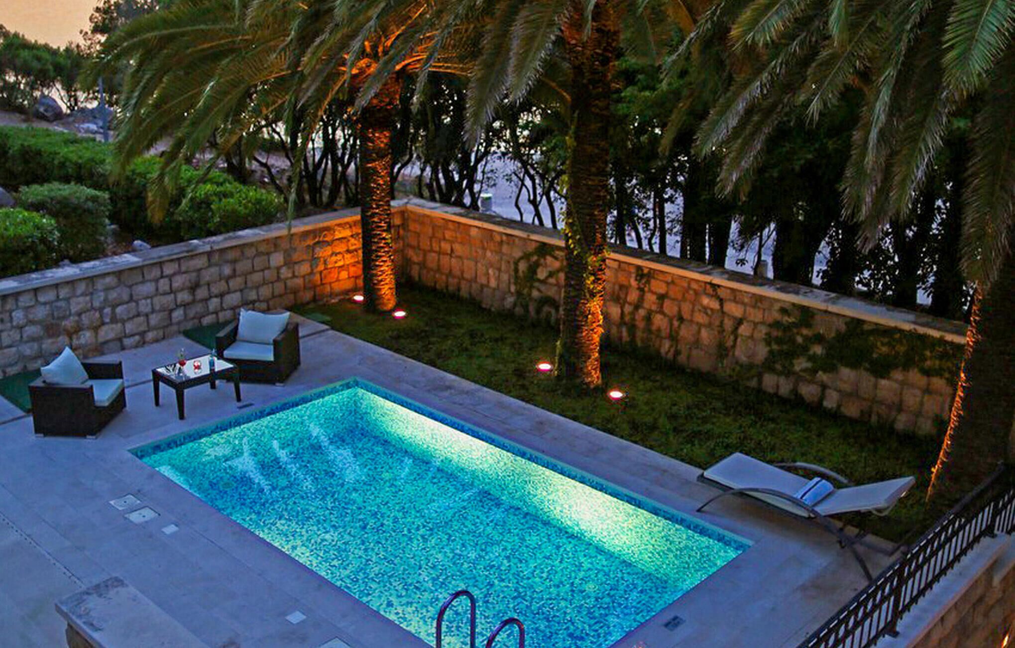 Una piscina rectangular amb un mur de pedra i palmeres.