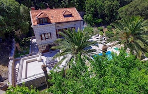 A two-story building with a tiled roof, surrounded by lush greenery and palm trees.