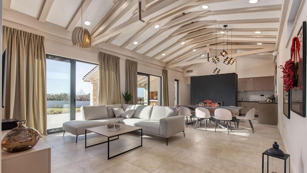 Een ruime woonkamer met een moderne zithoek, een eettafel met stoelen en een keukenruimte zichtbaar door een open deur.
