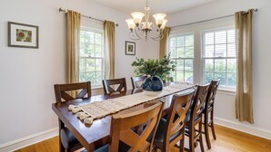Ein Esszimmer mit Holztisch, Stühlen, einer Chandelierleuchtre und einer Vase mit Grünpflanzen.