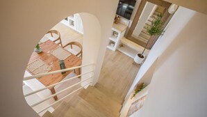 Zona de menjador amb taula i cadires de fusta, una escala i una planta en test.