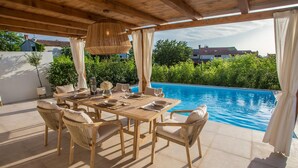 Zona de menjador exterior amb vista a la piscina, amb taula de fusta i cadires de vimet.