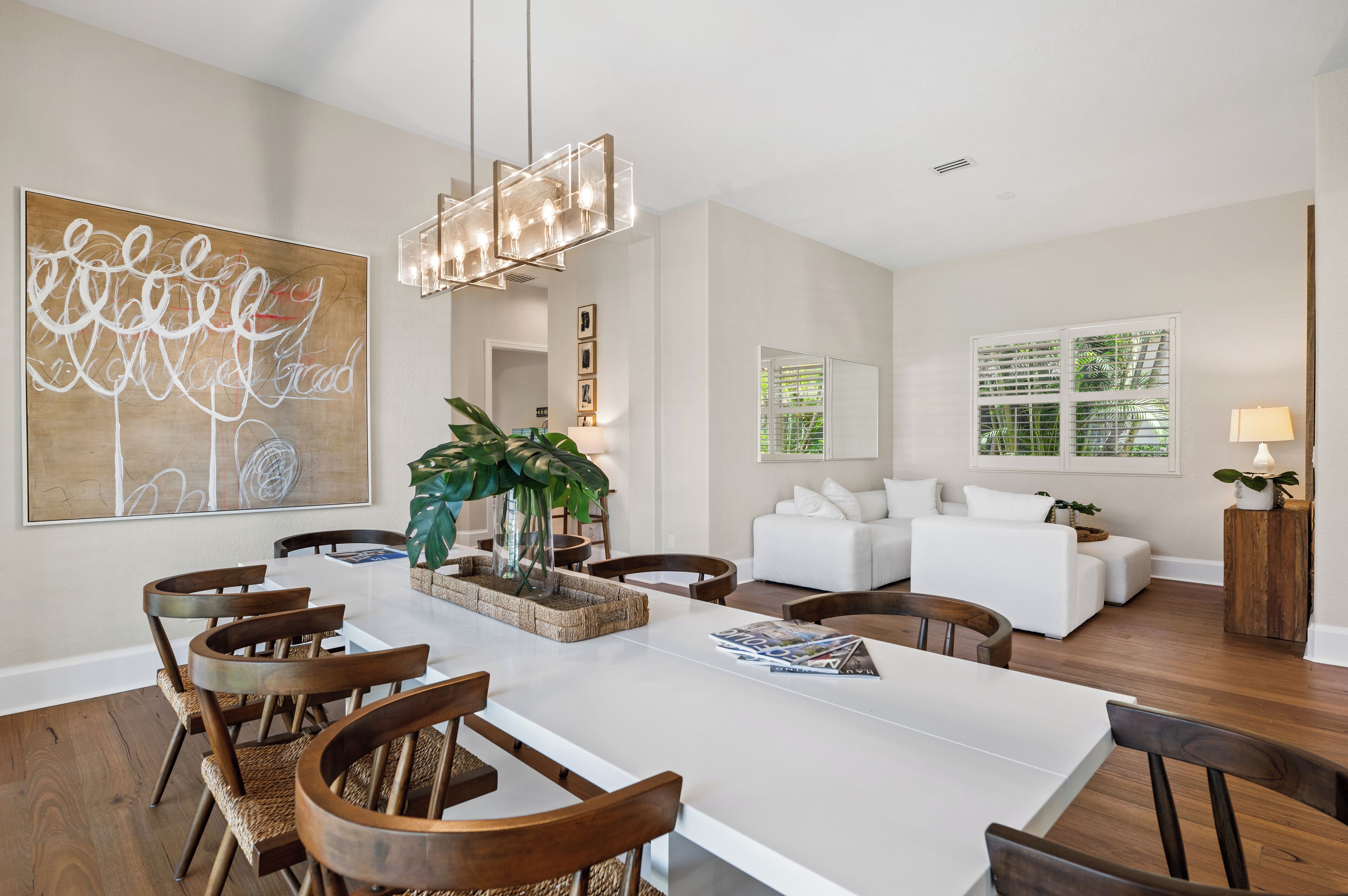 A spacious living area with a large dining table, white sofas, and a modern chandelier.