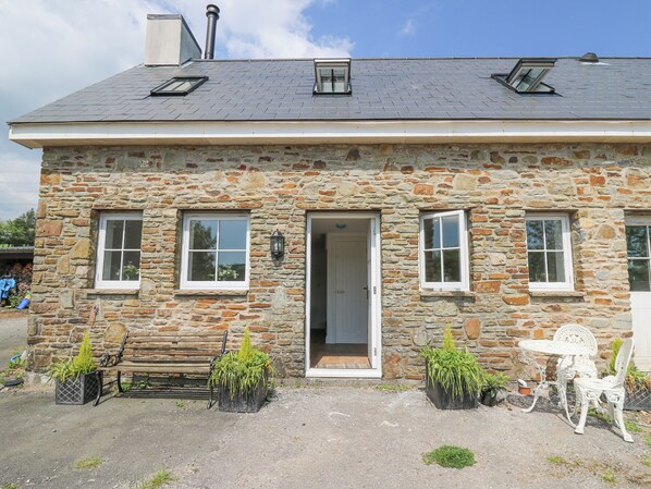 A stone building with a door, two windows, and a bench with potted plants.