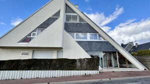 A modern, triangular-shaped building with a prominent sloped roof, a gated entrance, and a visible sign indicating 'LE GRAND LANE.' - Le Grand Large, 4-person apartment (Le Crotoy)
