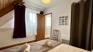 A bedroom with a bed, two rolled towels, a chair, a wooden door, and a window with curtains. - Le Grand Large, 4-person apartment (Le Crotoy)