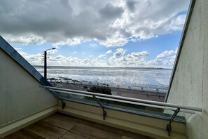 Varanda com guarda-corpo de vidro com vista para a orla marítima.
