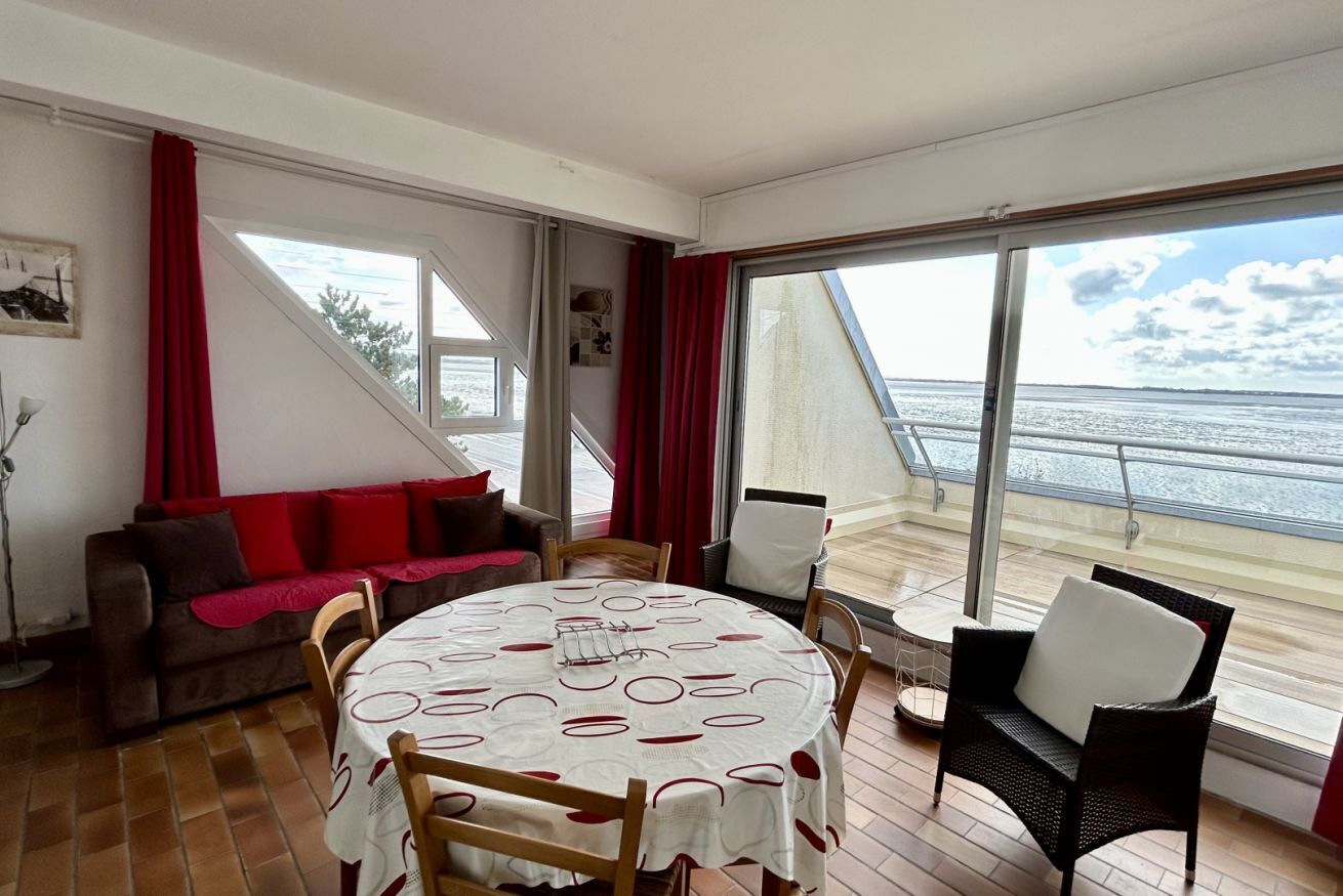 Een kamer met een ronde tafel, stoelen, een bank en grote ramen met uitzicht op zee.