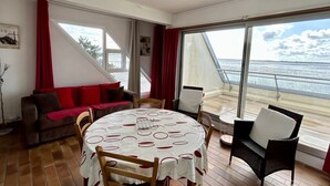 A room with a round table, chairs, a sofa, and large windows with a view of the sea. - Le Grand Large, 4-person apartment (Le Crotoy)