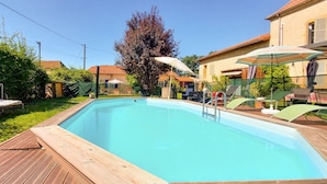 A rectangular swimming pool with a wooden deck, surrounded by outdoor furniture and umbrellas.