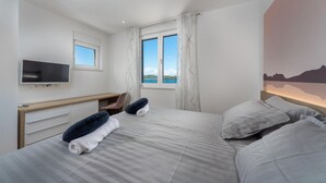 Una camera da letto con due letti, una scrivania, una televisione e una finestra vista mare.