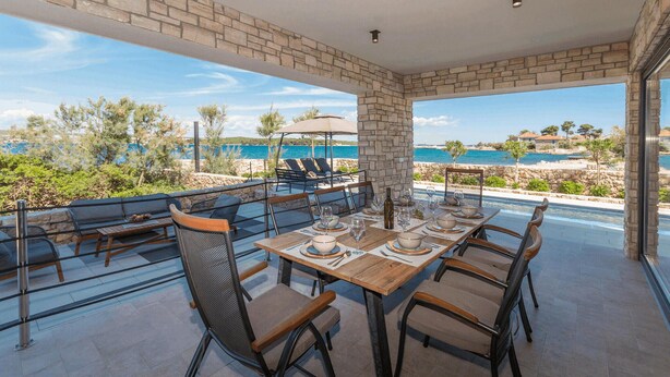 Zona pranzo con vista sul mare, pareti in pietra e posti a sedere all'aperto.