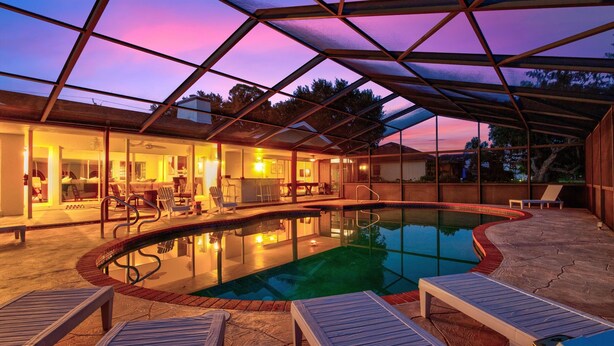 A covered swimming pool with lounge chairs, a bar area, and a view of the sunset. - 5BR/4BA |Pool & Spa + Pickleball, Golf View (Sarasota)