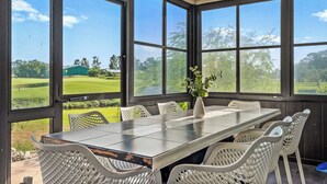 A covered dining area with a table and chairs, large windows offering a view of a golf course. - 5BR/4BA |Pool & Spa + Pickleball, Golf View (Sarasota)