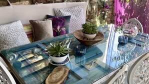 A cozy seating area with a glass-top table, white ornate chairs, and a stone wall backdrop. - Masal Küçükköy Otel (Ayvalik)