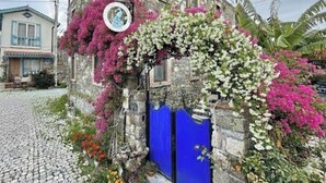 A stone building with a blue door, surrounded by lush pink and white flowering plants. - Masal Küçükköy Otel (Ayvalik)