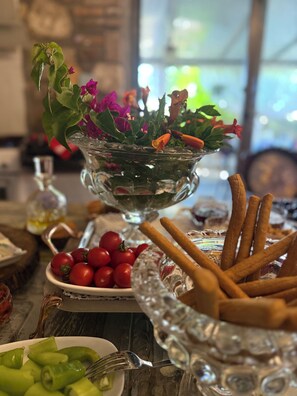 Ett bord med en glasskål full av blommor, en tallrik med körsbärstomater, en skål med gröna paprikor och en tallrik med kex.