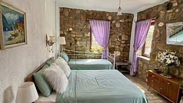 Un dormitorio con pared de piedra, dos camas, un aparador de madera y un cuadro en la pared.