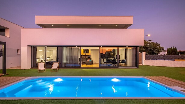 A modern two-story house with a swimming pool, large glass doors leading to a living area, and a well-maintained lawn.