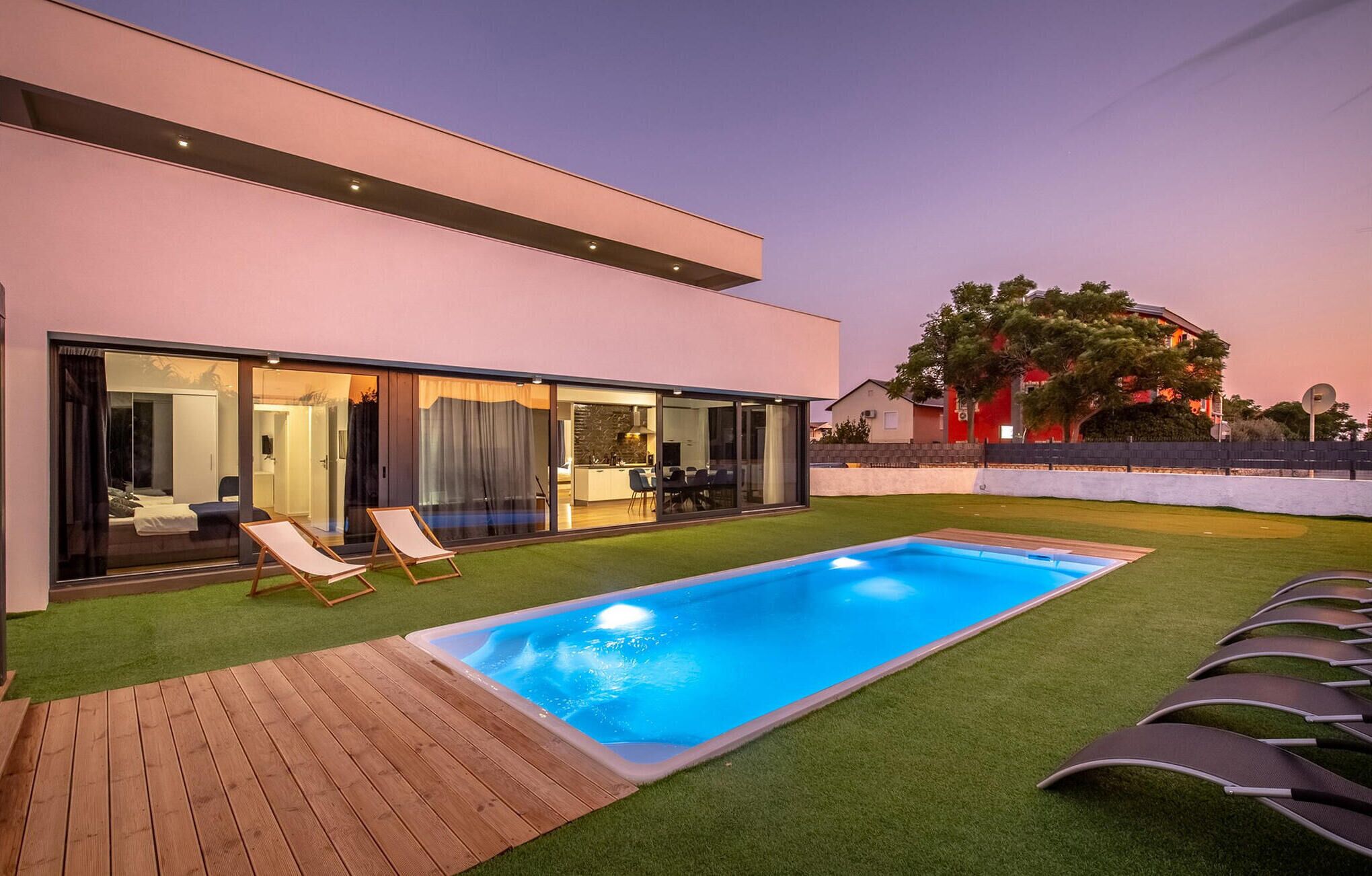 A modern house with a swimming pool, a wooden deck, and a glass-enclosed patio area.